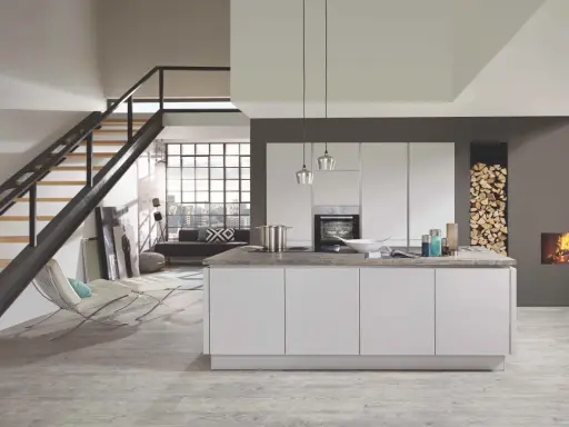 Cuisine moderne avec îlot central blanc. Le mur gris foncé contraste avec les meubles blancs et le bois de chauffage.