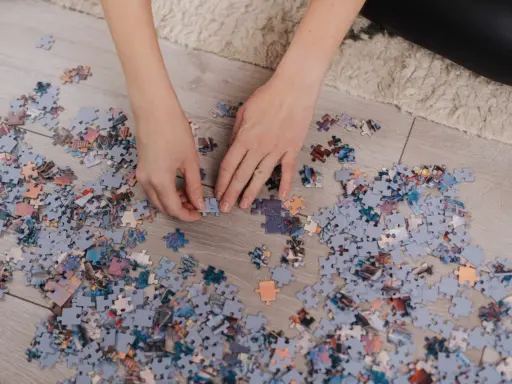 Ręce układają puzzle na podłodze. Po skończeniu dowiesz się, jak powiesić puzzle na ścianie.