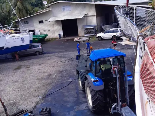 Tracteur bleu près d'un bateau, peut-être pour le prix d'entretien d'un bateau de 7m. Des ouvriers travaillent.