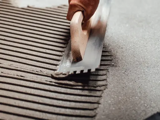 Application d'enduit pour carrelage avec une taloche crantée, assurant une épaisseur carrelage et colle uniforme pour une pose parfaite.
