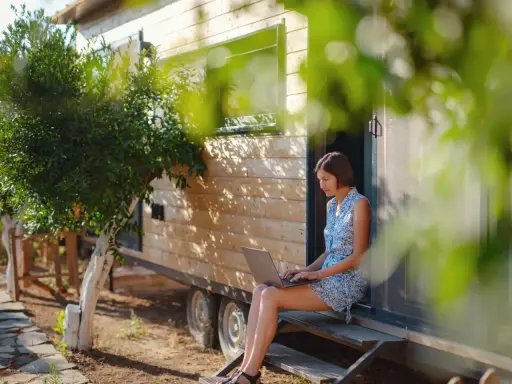 Frau arbeitet auf Laptop vor einem Tiny House. Ein Beispiel für modernes, flexibles wohnen in der zukunft.