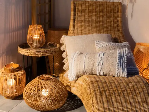 Przytulny balkon w stylu boho z wiklinowymi latarenkami, poduszkami i leżakiem.