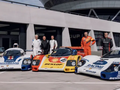 Fünf Rennfahrer stehen stolz neben ihren Porsche-Rennwagen der Gruppe C.