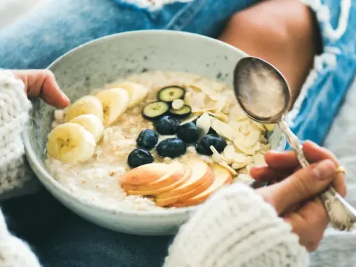 Schüssel mit Haferflocken, Bananen, Blaubeeren und Mandelsplittern. Ein Löffel wartet darauf, die gesunde Mahlzeit zu genießen, die nicht dick machen muss.