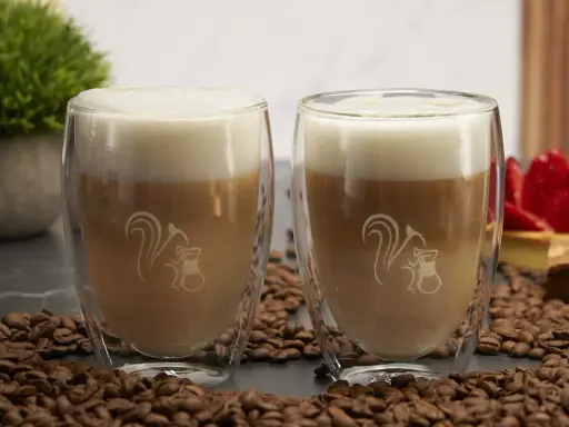 Zwei Latte Macchiato im Glas, umgeben von Kaffeebohnen. Ein typischer Latte Macchiato hat ca. 250-300 ml.