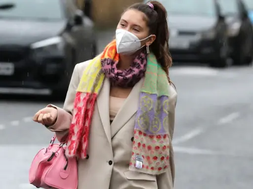 Iris Law, con mascarilla y bufanda multicolor, camina por la calle con un bolso rosa.
