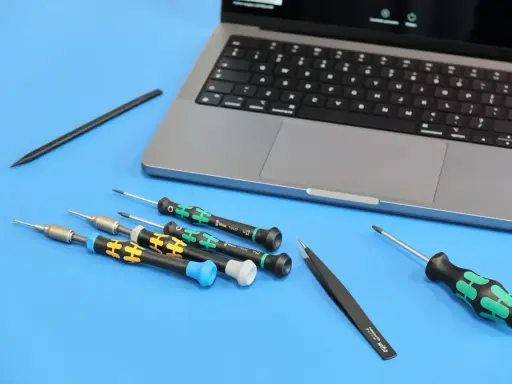 Narzędzia do naprawy iPhone'a: precyzyjne śrubokręty i pęseta obok laptopa. Przygotowanie do serwisu.