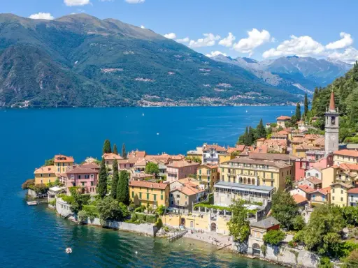 Färgstarka hus vid en azurblå sjö, omgivna av gröna berg. Ett perfekt exempel på mysiga resmål i Italien.