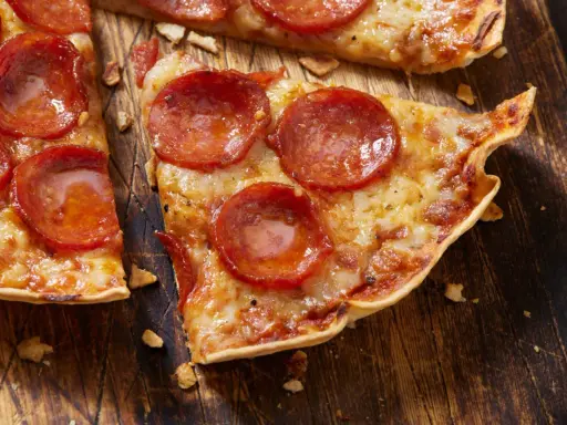 Pyszna pizza na tortilli z pepperoni, roztopionym serem i chrupiącym spodem, podana na drewnianej desce.