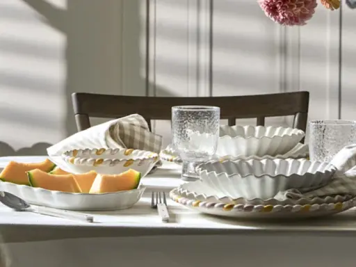 Ett dukat bord med en fin servis, frukt och blommor. Vackra vita skålar med vågiga kanter och glas med textur.