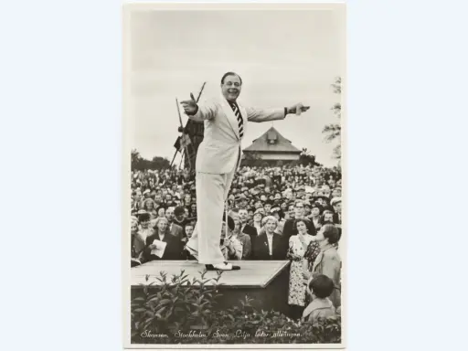Sven Lilja leder allsången på Skansen. En glad publik lyssnar.