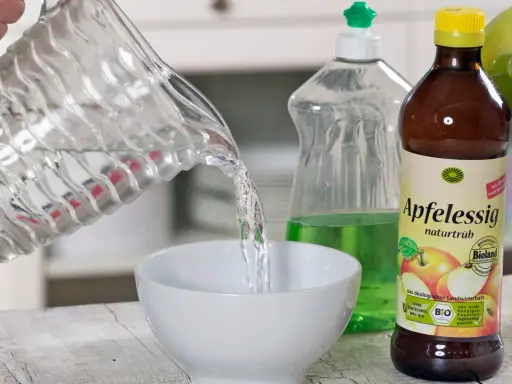 Wasser wird in eine Schüssel gegossen, um eine Fruchtfliegenfalle zu bauen. Apfelessig und Spülmittel sind bereit.
