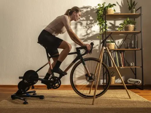 Frau trainiert auf einem Heimtrainer, was ist spinning? Sie tritt kräftig in die Pedale, während im Hintergrund ein Regal mit Pflanzen und Büchern steht.