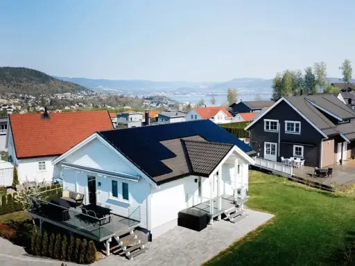 Vackra hus med solpaneler på taken, en del av ett system med Growatt 8000TL3-XH, i ett soligt bostadsområde med utsikt över en sjö.
