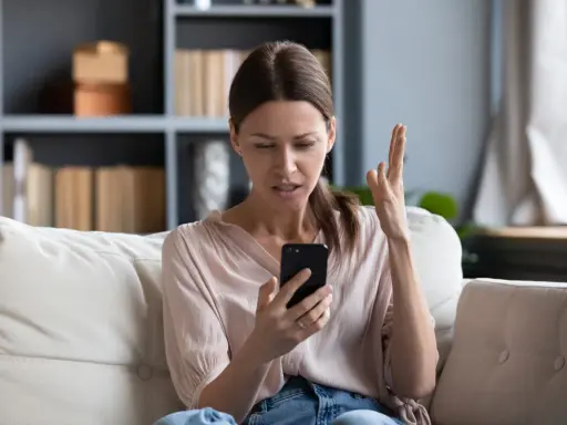 Zirytowana kobieta próbuje włączyć internet w telefonie, gestykulując z frustracją.