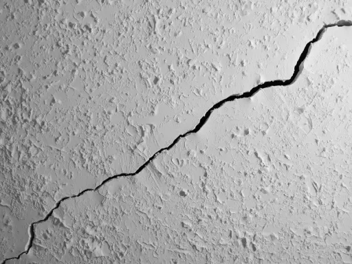 Gros plan sur une fissure traversant un plafond texturé. La fissure est sombre et profonde, contrastant avec la surface blanche et irrégulière.