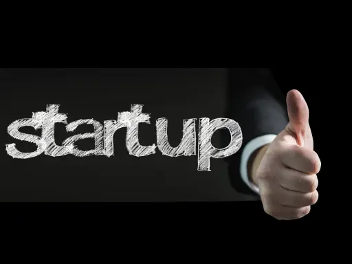 Słowo "startup" napisane kredą na czarnym tle, obok kciuk w górę. To symbol sukcesu w biznesie.