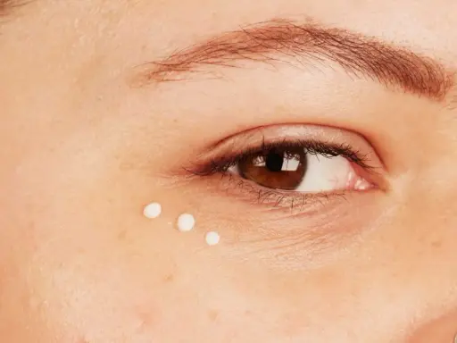 Trois petites perles de crème sont appliquées sous l'œil, montrant comment appliquer contour des yeux pour une peau hydratée.