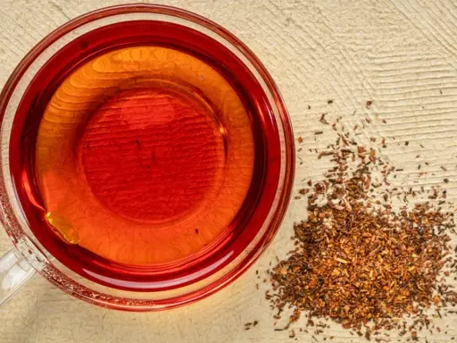 Eine Tasse roter Rooibos Tee neben getrockneten Blättern. Ideal für die Schwangerschaft.
