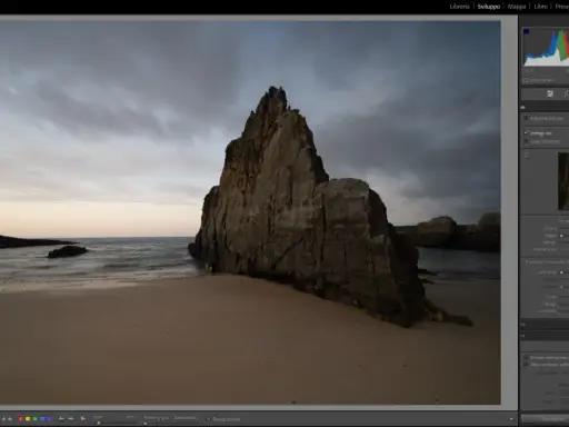 Scogliera imponente su una spiaggia al tramonto, con onde mosse. L'aggiornamento Lightroom sta migliorando i dettagli dell'immagine.