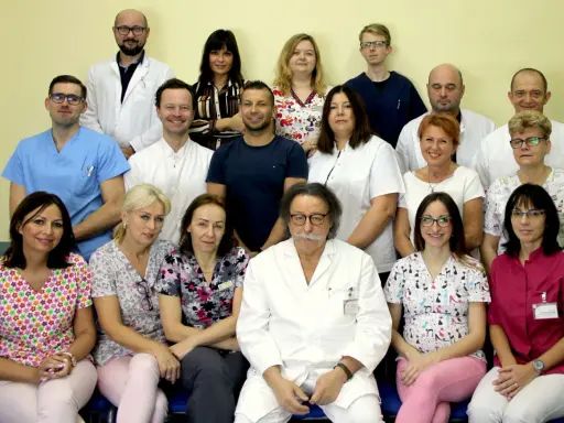 Grupa lekarzy i pielęgniarek w białych fartuchach i kolorowych strojach medycznych, pozująca do zdjęcia.