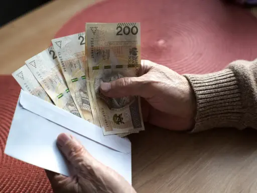 Dłoń trzyma kopertę z banknotami 200 zł. Czy to pieniądze na 800 plus do jakiegoś wieku?