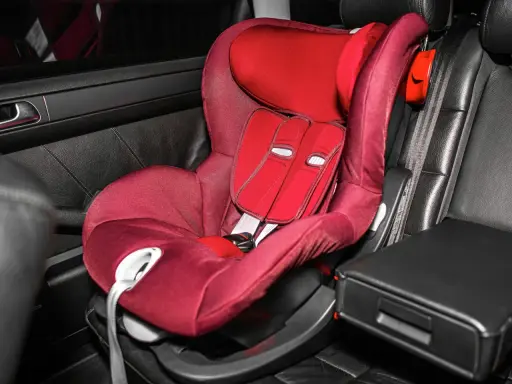 Silla de coche roja en asiento de cuero negro. Las sillas Isofix se pueden poner con cinturón, ofreciendo versatilidad para la seguridad infantil.