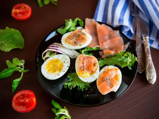 Jajka na twardo z łososiem i sałatą, idealne na dietę low carb. Pomidorki i zioła dopełniają danie.