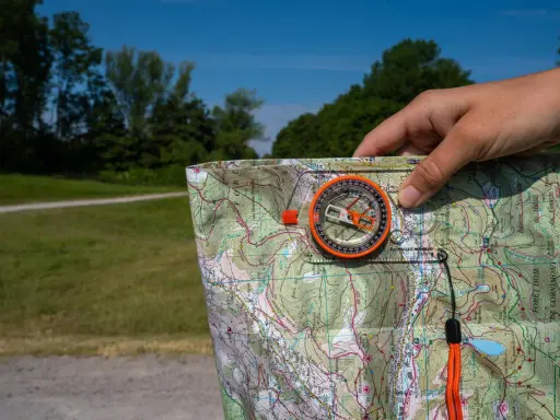 Dłoń trzyma mapę i kompas, pokazując, jak działa kompas w terenie.