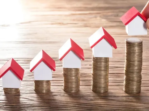 Cinq maisons miniatures sur des piles de pièces, symbolisant une augmentation du loyer sur 3 ans.