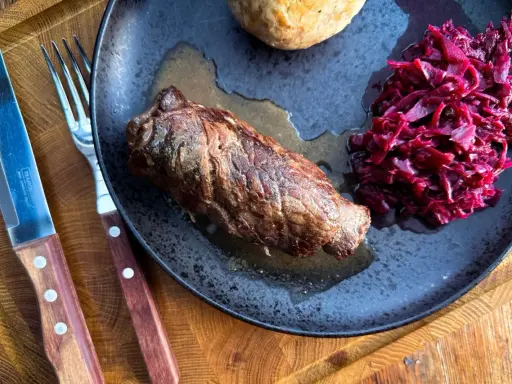 Herzhafte Rouladen im Dutch Oven zubereitet, serviert mit Rotkohl und Klößen auf einem rustikalen Teller.