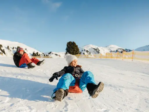 Bambini felici scendono con slittino su pendio innevato. L'altitudine neonati non è un problema per queste avventure invernali.