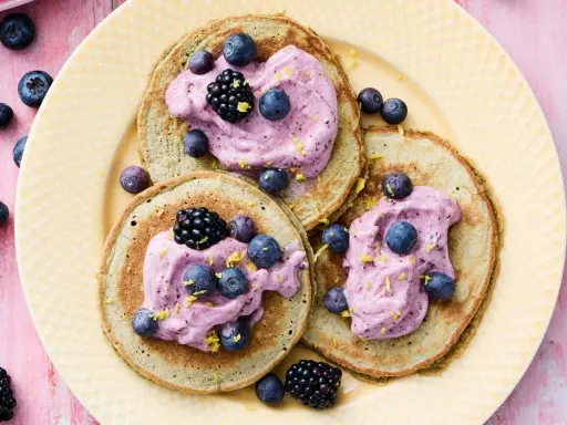 Tre fluffiga pannkakor med havregryn toppas med lila grädde, blåbär och björnbär. Strössel av citronskal ger en frisk touch.