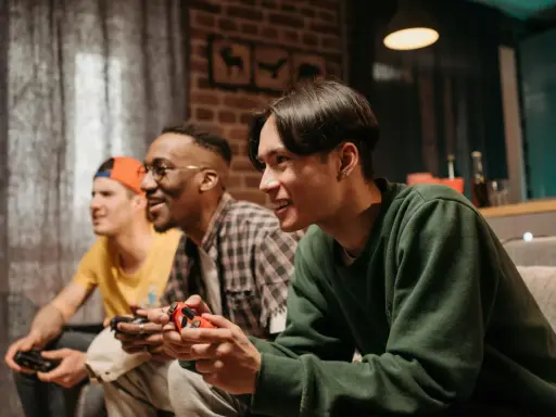 Trzech przyjaciół gra w darmowe gry na PS4, śmiejąc się i rywalizując.