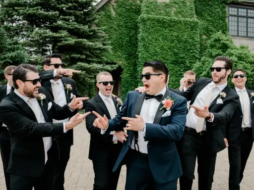 Groomsmen in black suits and cream ties, with the groom in a navy suit, all sporting sunglasses and a playful mood. Do groomsmen match the groom? Not exactly, but they're all dressed to impress!