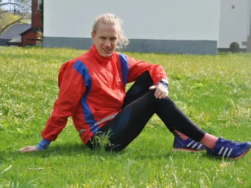 En löpare i röd jacka och svarta tights vilar i gräset, redo att springa milen under 50 minuter.