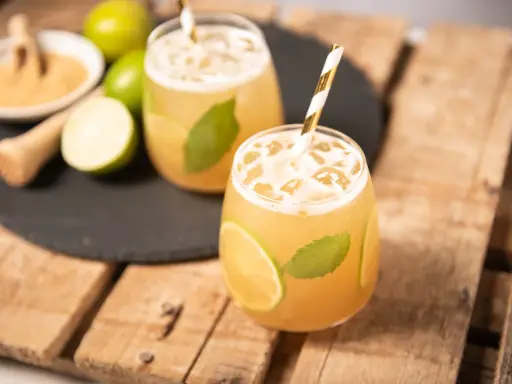 Erfrischender cocktail mit braunem rum, Limette und Minze, serviert mit Eis und einem gestreiften Strohhalm.