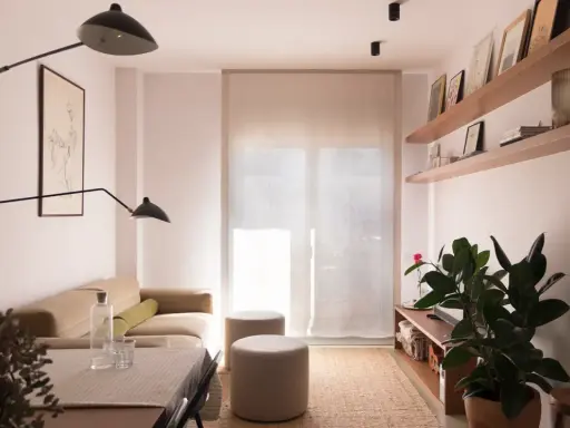 Salón moderno con sofá beige, mesa y dos pufs. Las paredes lucen un impecable **microcemento acabado**, aportando elegancia y minimalismo.