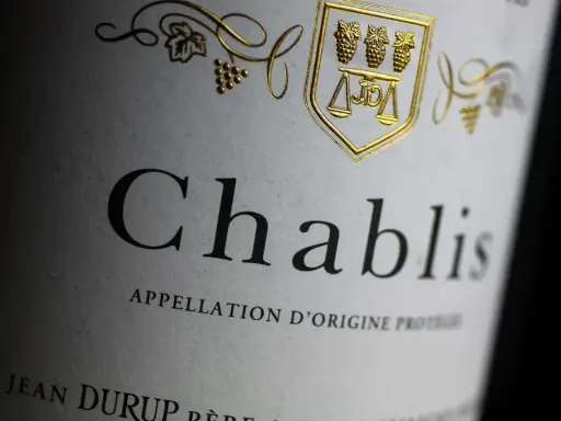 Nahaufnahme eines Etiketts mit der Aufschrift "Chablis". Ein goldenes Wappen mit Trauben und Waage ziert das Etikett dieses Chablis Weins.