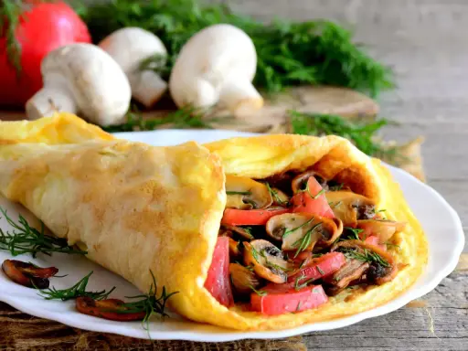 Złocisty omlet z pomidorami i pieczarkami, udekorowany koperkiem. Pyszne śniadanie na drewnianym blacie.