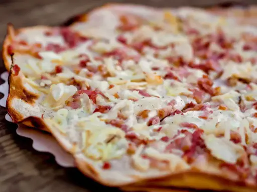 Tarte flambée gourmande, spécialité d'un restaurant alsacien à Nantes. Crème, lardons et oignons sur une pâte fine et croustillante.