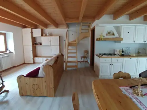 Come arredare una taverna: cucina bianca, divano in legno, scala a vista e soffitto a travi.