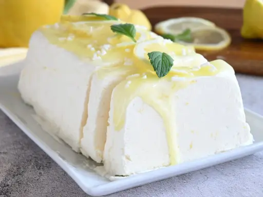 Un delizioso semifreddo al limone, guarnito con scorzette, menta e una glassa gialla, pronto per essere gustato.