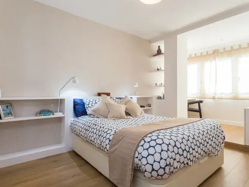 Habitación moderna con cama, estanterías y una apertura que permite tirar tabique para unir dos habitaciones.