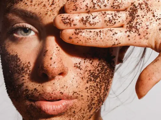 Visage couvert de grains d'un exfoliant chimique naturel, une main cache un œil.