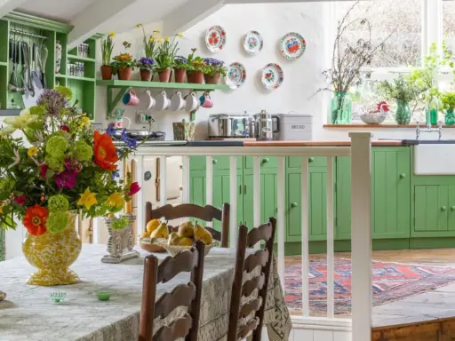 Cuisine lumineuse avec armoires vertes, bouquet de fleurs coloré sur la table, et vaisselle décorative. Ambiance chaleureuse de deco cottage chic.