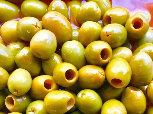 Un primer plano de muchas aceitunas verdes, algunas deshuesadas, listas para ser parte de las clases de aceitunas para comer.