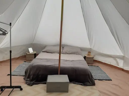 Komfortowy glamping nad morzem: łóżko z pościelą, stoliki nocne, wieszak i namiot.