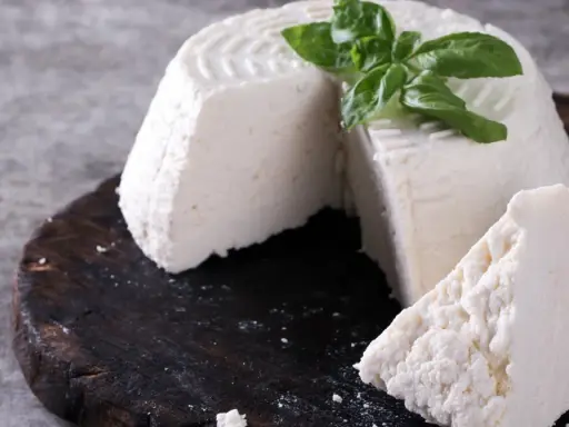 Świeża ricotta z bazylią na ciemnej desce.
