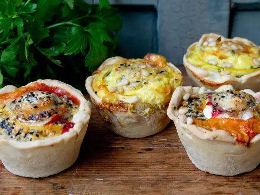 Vier köstliche Mini-Quiches mit verschiedenen Füllungen, perfekt für ein schnelles mini quiche rezept. Mit Petersilie garniert.